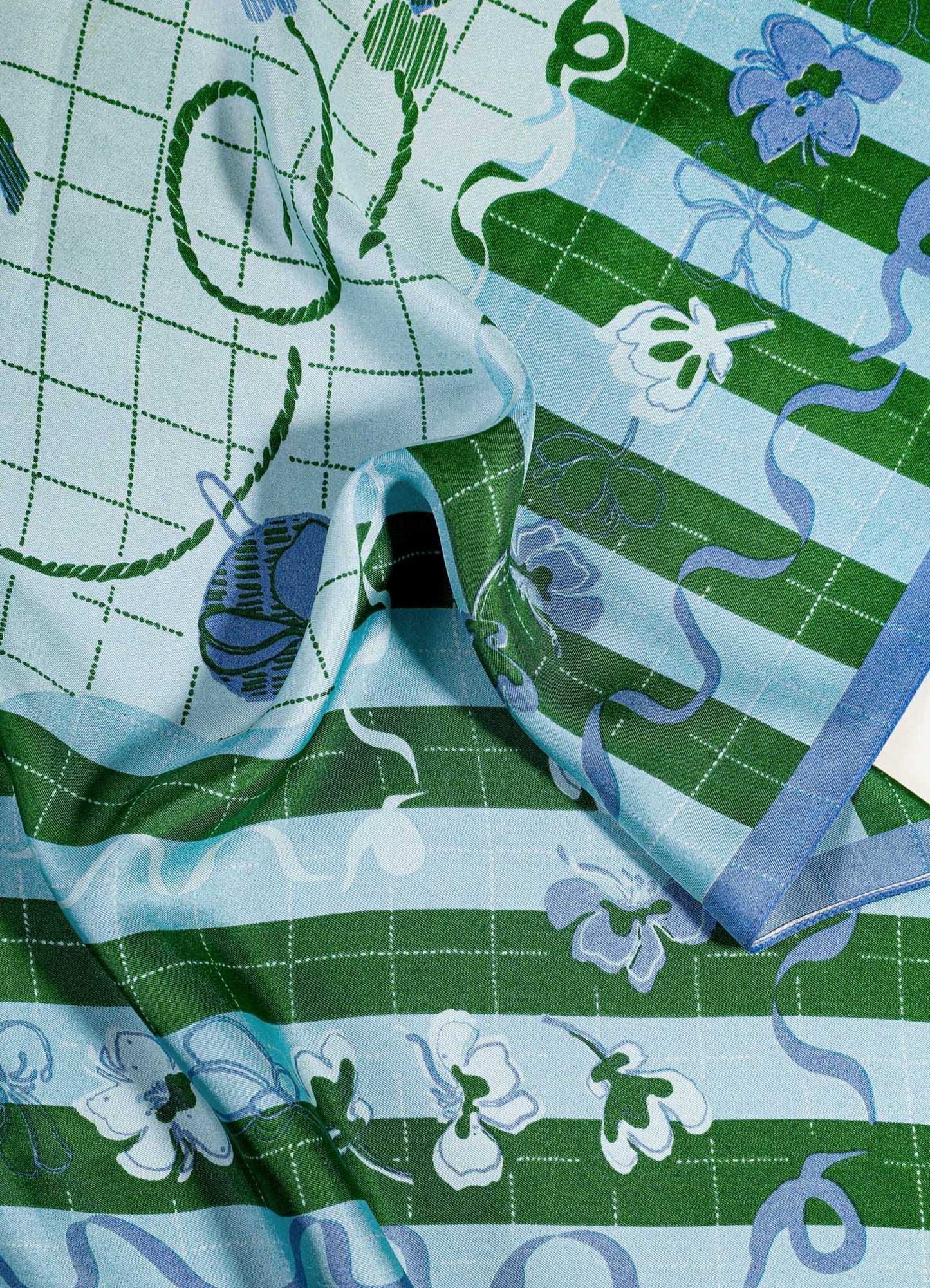 Cotton fabric with a botanical pattern of white flowers and green stripes, featuring a grid design and decorative ribbon motifs in shades of blue and green. The material appears lightweight with a smooth, flowing texture.
