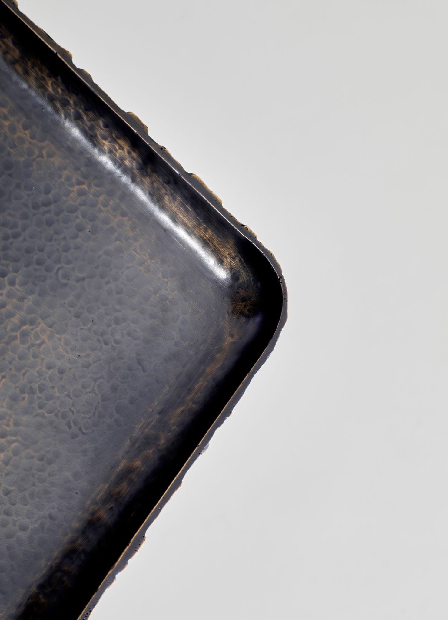 A close-up of a rectangular metal tray with a hammered texture and antique brass finish, featuring slightly rounded edges on a plain, light-colored background.
