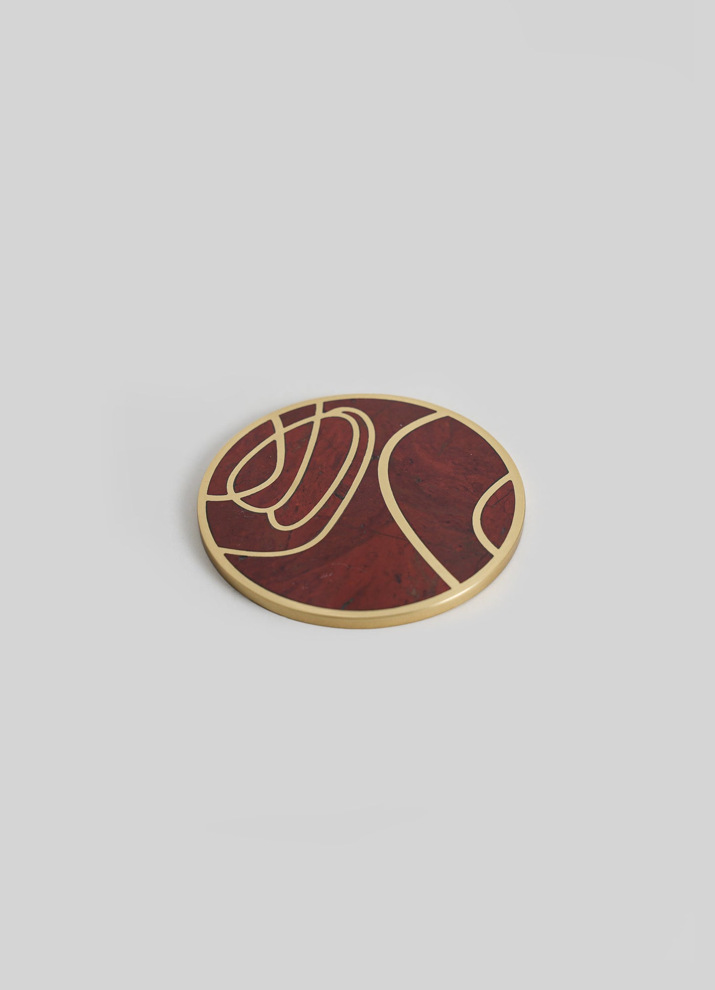 A round coaster with a geometric pattern in red and gold, featuring curved lines and sections, made from a material resembling marble or resin with a metallic finish.