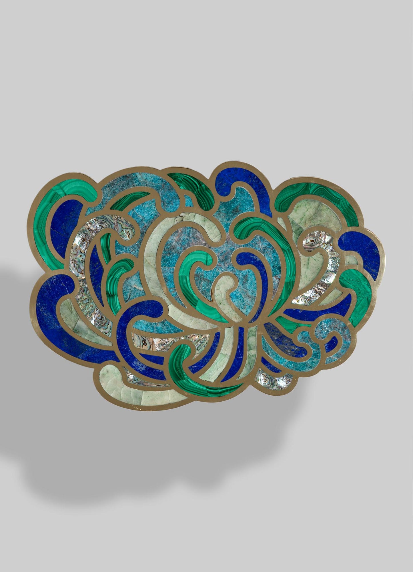 Decorative inlay piece featuring swirling patterns in shades of blue, green, and cream, outlined with metallic borders, made from inlaid stone or shell materials. The design has an abstract motif with a combination of polished and textured surfaces, evoking craftsmanship and artisanal style.