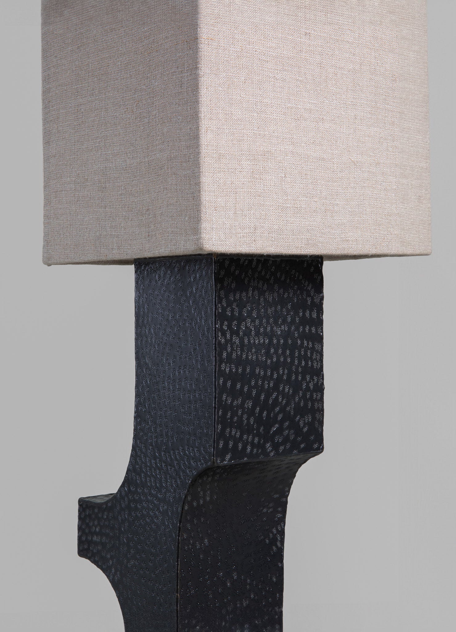 Close-up of a table lamp featuring a fabric lampshade in neutral beige tones and a black ceramic base with a textured, dotted pattern. The design combines contemporary style with minimalist elegance.