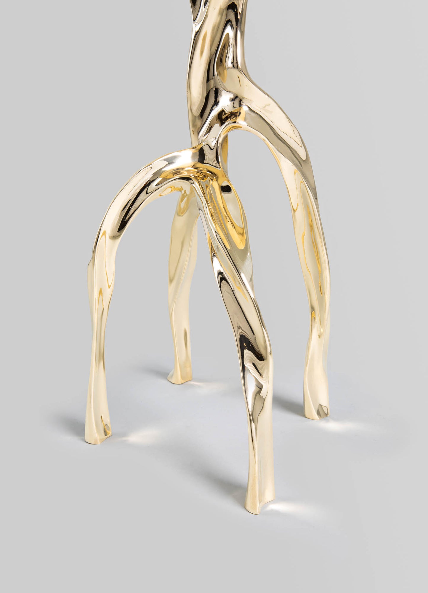 A decorative table sculpture made of polished brass with an organic, twisting form resembling intertwined branches or roots, featuring a reflective metallic finish.