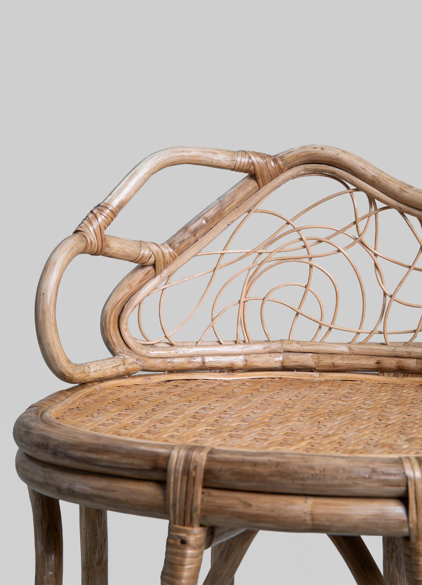 Wicker chair with a curved wooden frame, wicker woven seat, and an intricate rattan backrest featuring swirling circular motifs, set against a plain gray background.