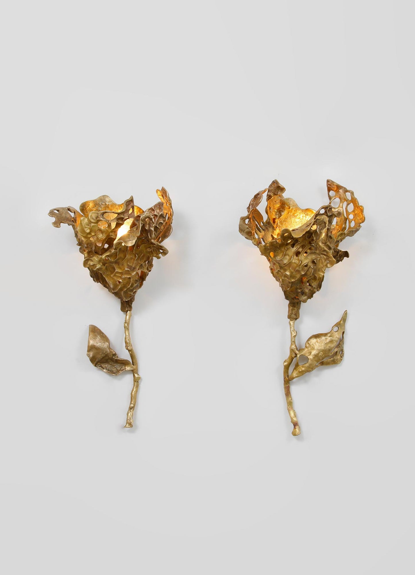 Gold-toned metal wall sconces with abstract, organic floral motifs and textured, sculptural design, mounted on a plain background.