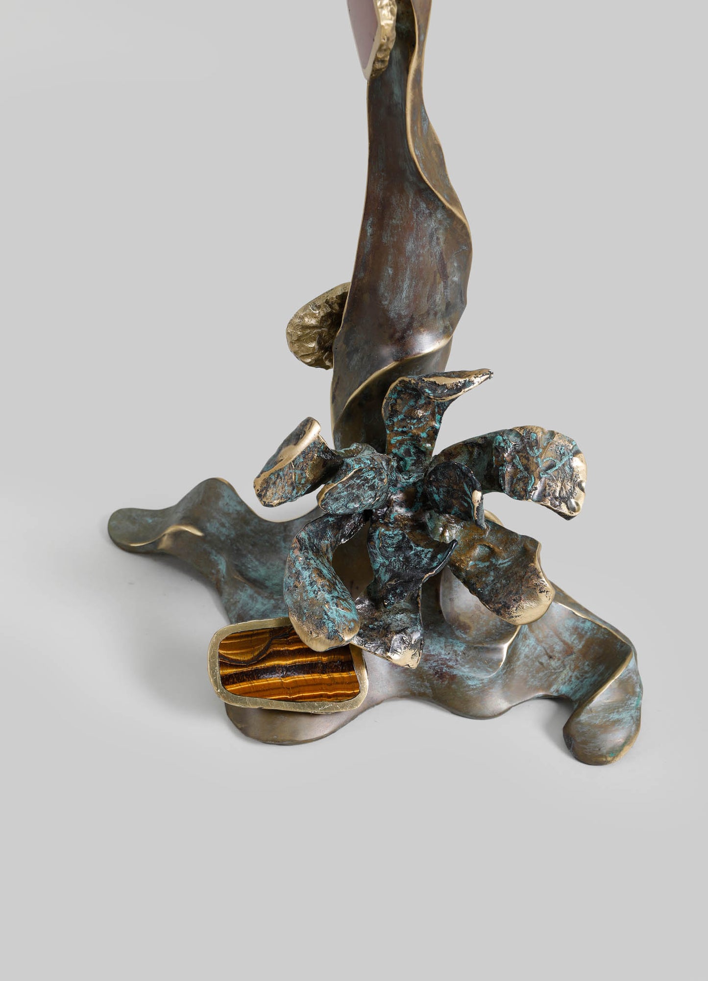 Decorative sculpture with a rustic, handcrafted style featuring abstract, organic forms in bronze and patina finishes, including a pop of tiger's eye gemstone at the base.