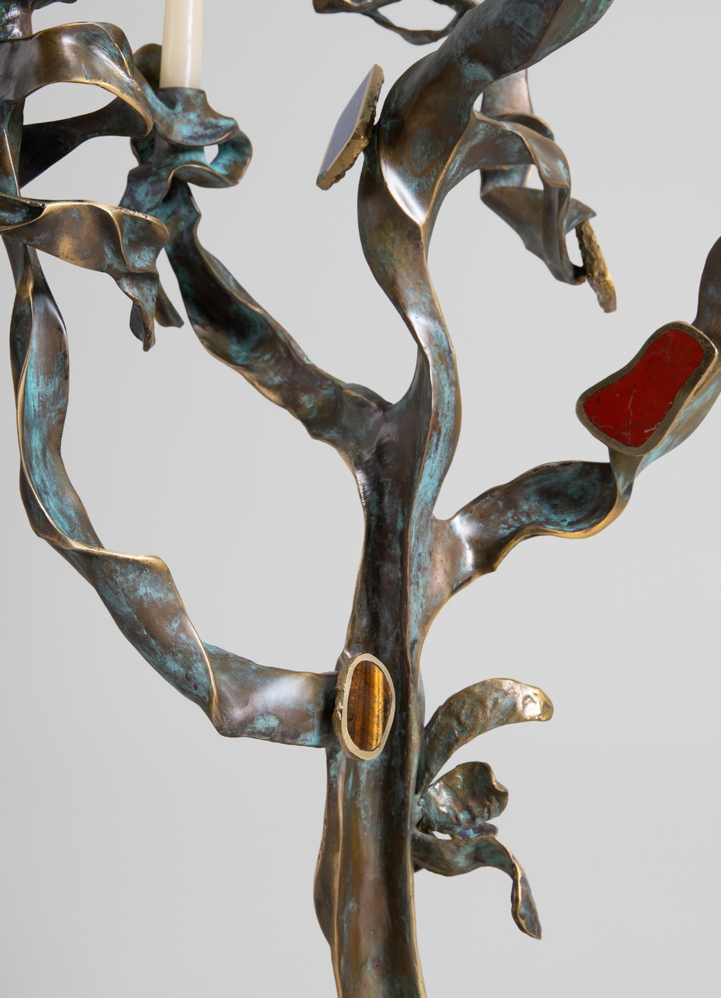 A metal wall sculpture with a botanical design featuring twisting, leaf-like shapes in a weathered bronze finish, accented with red and amber resin inlays. The sculpture has an organic, handcrafted style with a rustic and artistic mood.