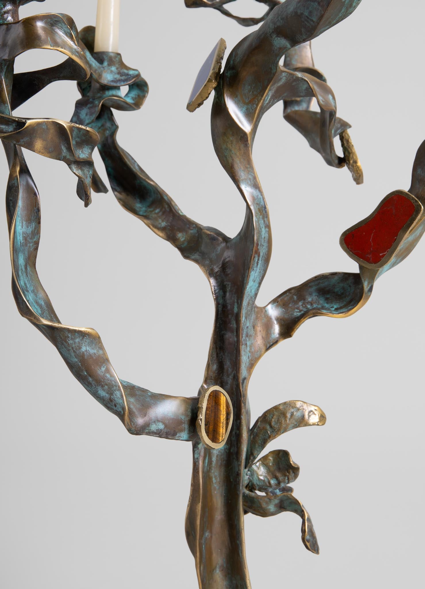 A metal wall sculpture with a botanical design featuring twisting, leaf-like shapes in a weathered bronze finish, accented with red and amber resin inlays. The sculpture has an organic, handcrafted style with a rustic and artistic mood.