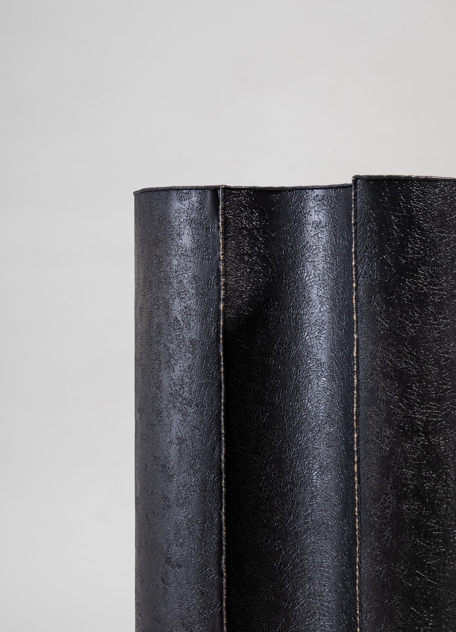 A textured black leather cushion with a subtle pebbled pattern, featuring visible topstitching along the edges. The cushion appears to be rectangular and has a contemporary style.