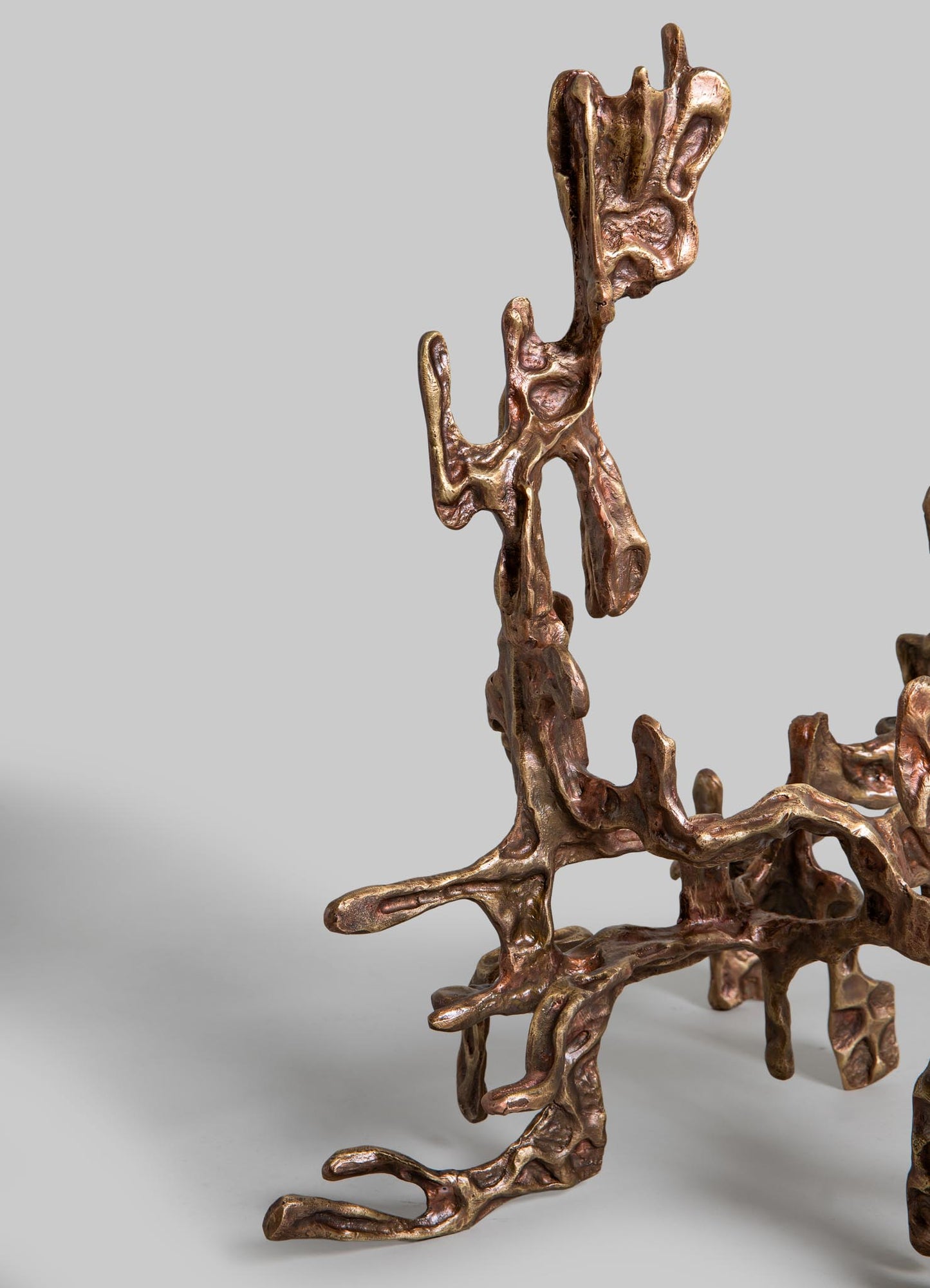 A metallic sculpture with an organic, abstract form in a bronze or copper finish, featuring flowing, irregular shapes and textured surfaces. The sculpture has a contemporary style, emphasizing fluidity and natural motifs.