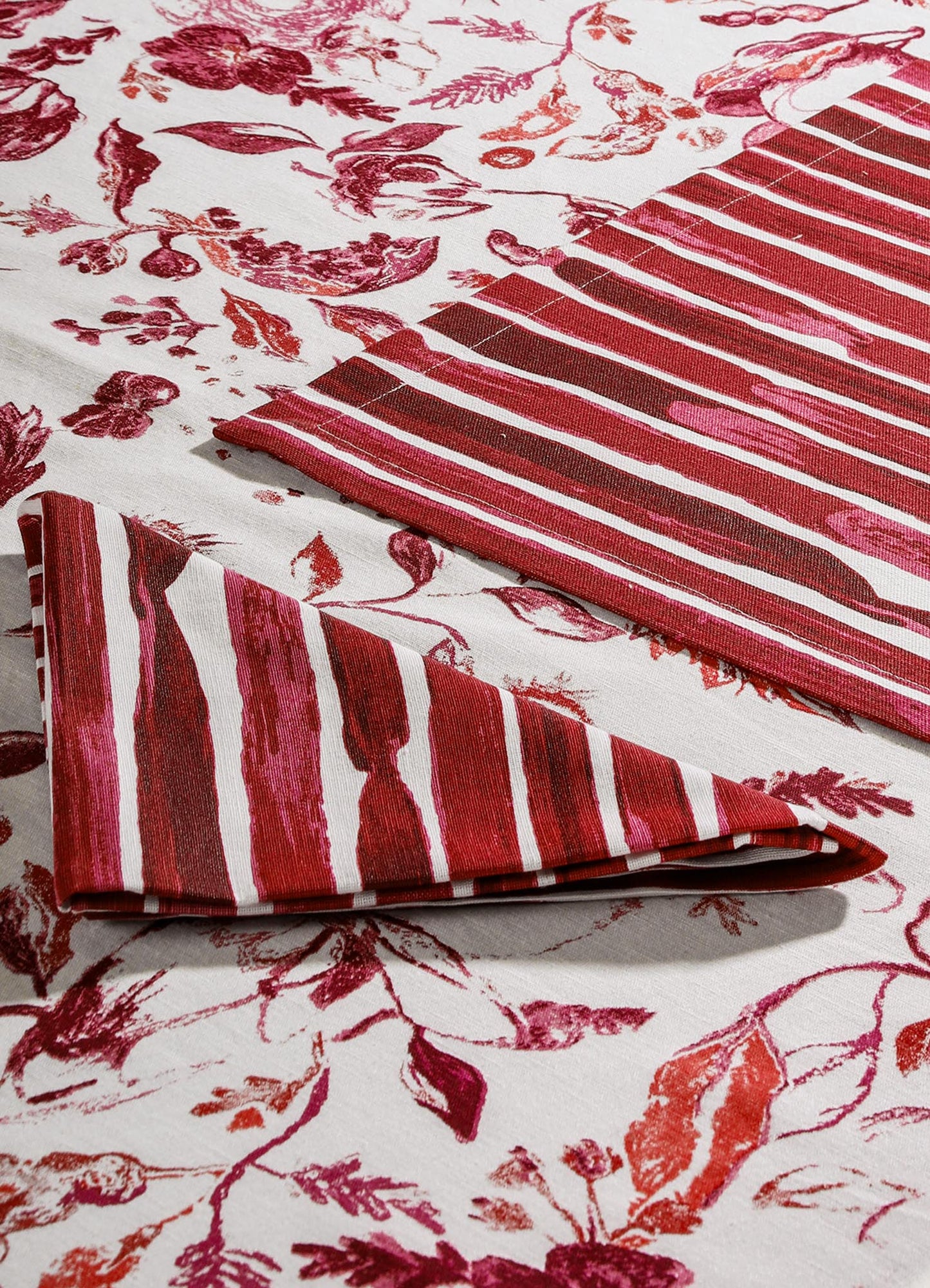 Cotton tablecloth with a floral print in shades of red and pink, featuring a striped border pattern. The fabric has a natural, textured appearance suitable for casual or elegant dining settings.