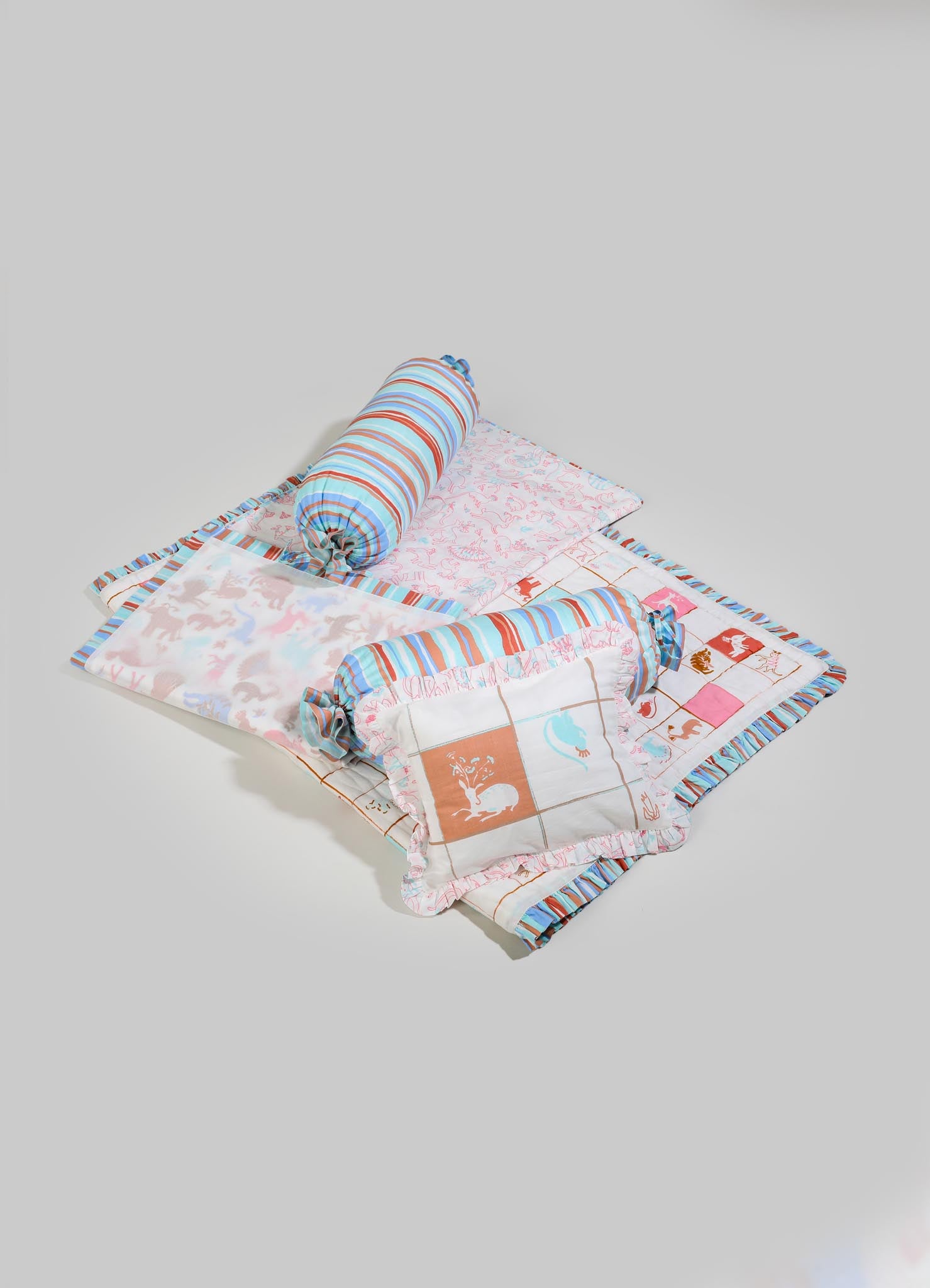 Children's bedding set with patterned quilt, matching pillowcases, and a cylindrical bolster cushion in pastel pink, blue, and orange tones, featuring animal and floral motifs. The set is made of lightweight fabric with striped and printed designs.