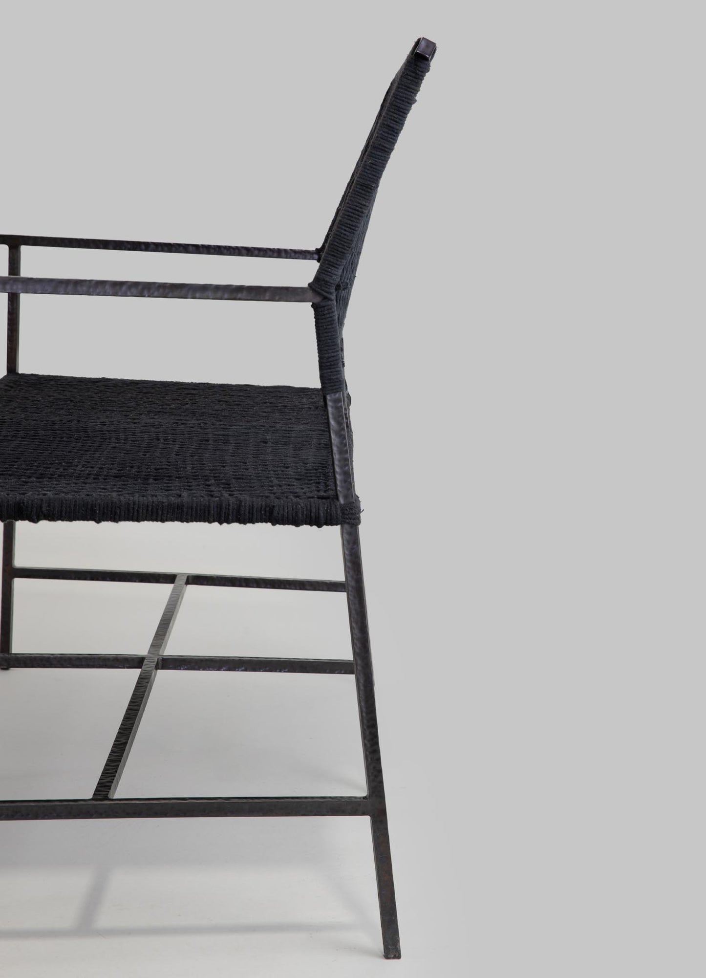 A black metal chair with woven rattan or wicker seat and backrest, featuring slim, angular legs and a minimalist design.