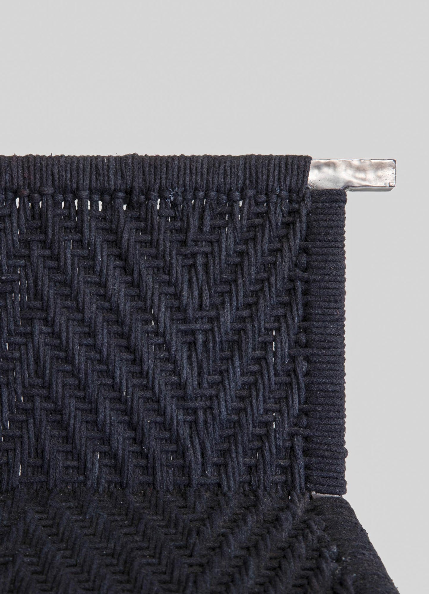 Woven textile with a dark navy color featuring a textured, geometric pattern and finished with a silver metal detail at the top. The style appears contemporary with a focus on tactile design and craftsmanship.