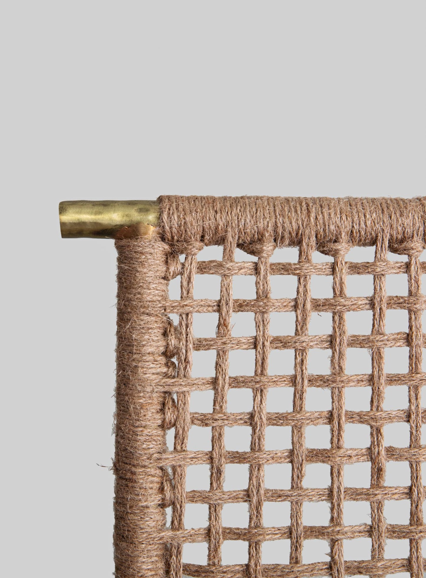 Wicker or rattan chair with a woven grid pattern, featuring a brass or gold-colored metal top rail, set against a plain background.