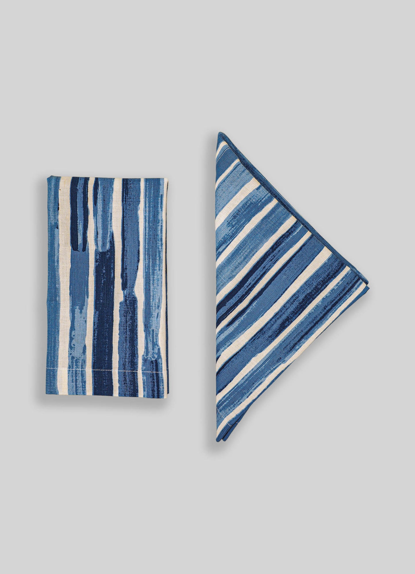 Blue and white striped fabric napkins with a hand-painted watercolor pattern, made from cotton or linen. The design features varying vertical and diagonal stripes, creating a casual yet refined look.