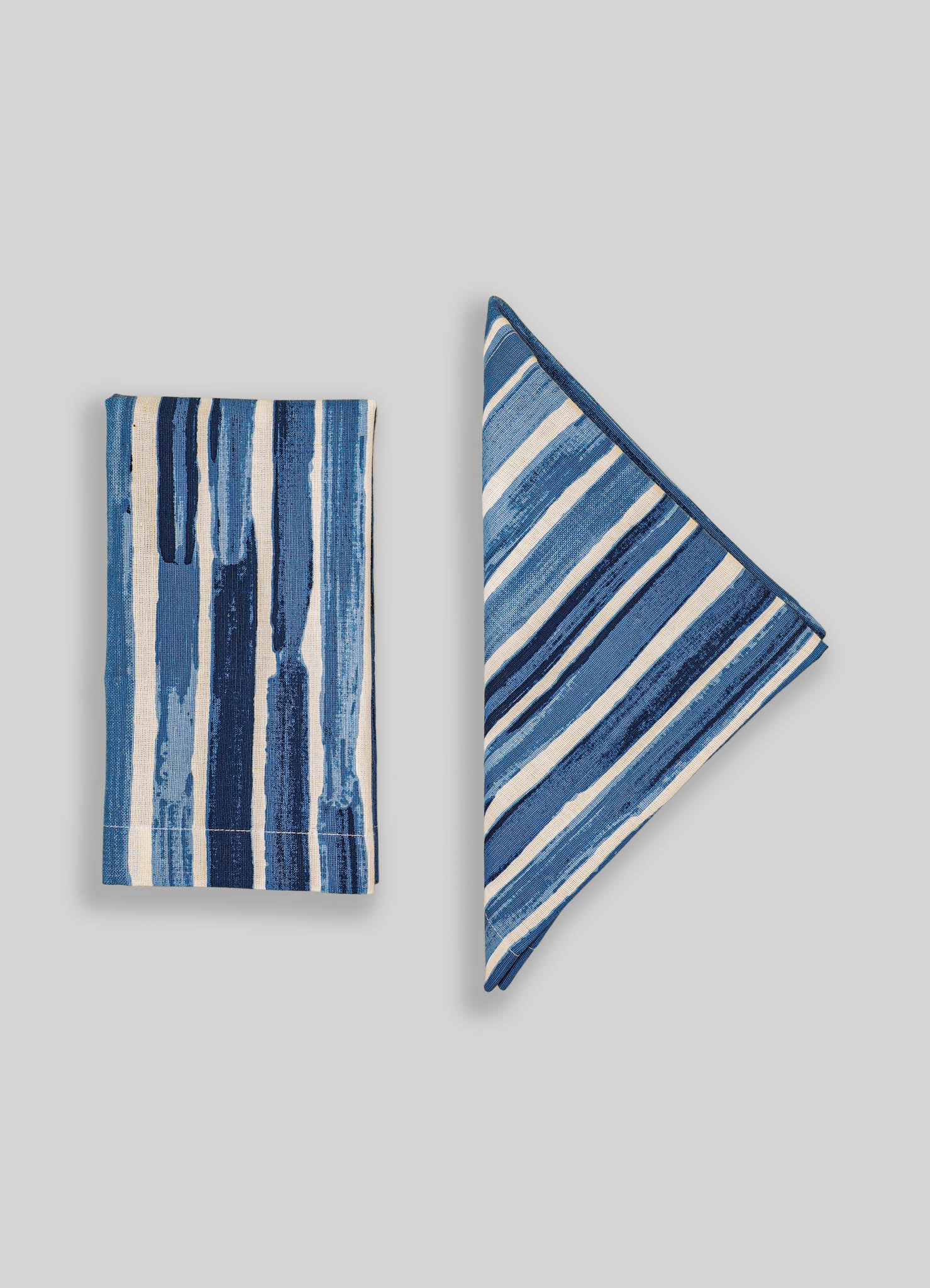 Blue and white striped fabric napkins with a hand-painted watercolor pattern, made from cotton or linen. The design features varying vertical and diagonal stripes, creating a casual yet refined look.