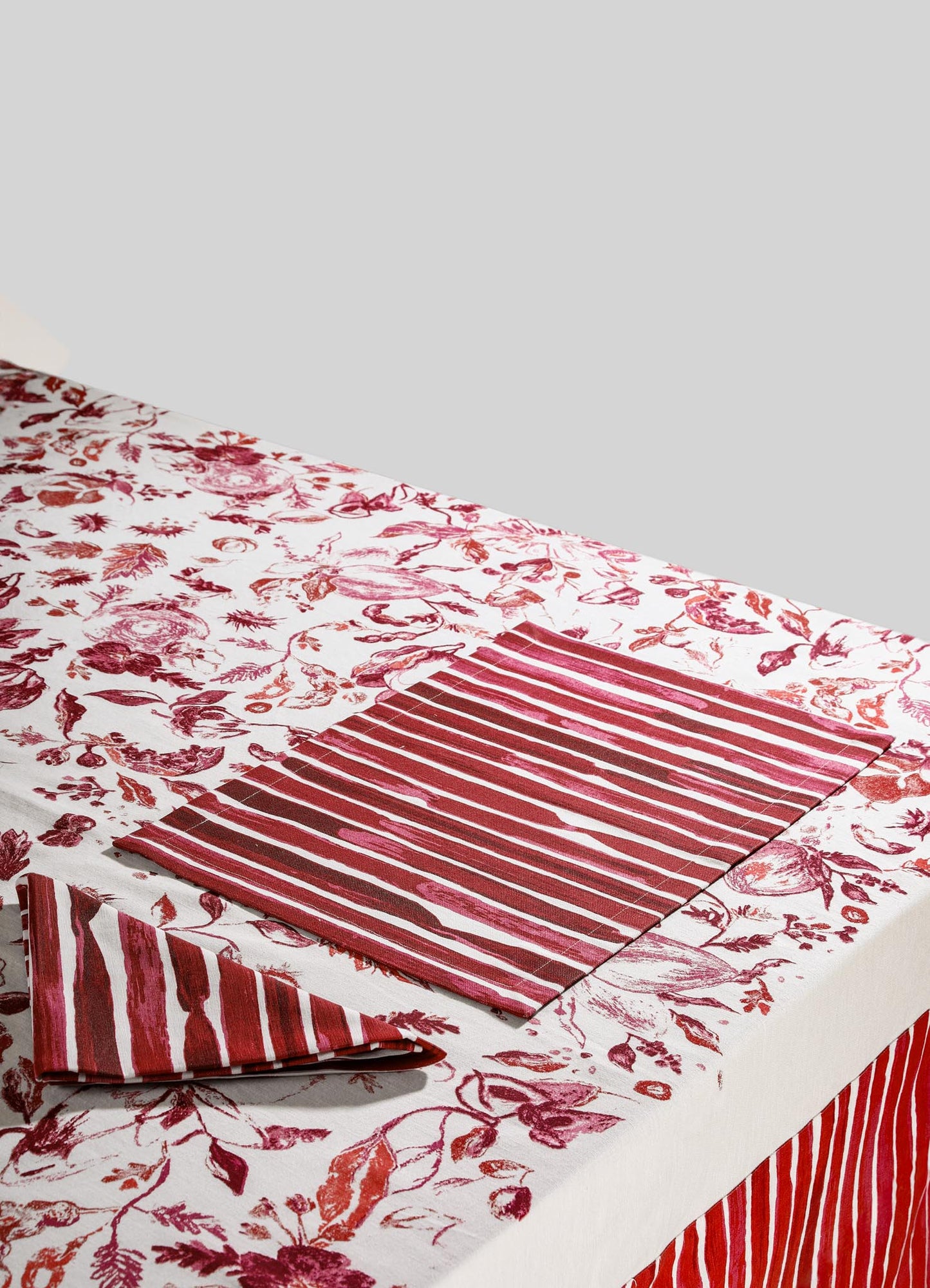 Printed cotton tablecloth with a floral motif and a red and white striped fabric placemat, featuring botanical illustrations and a rustic style.