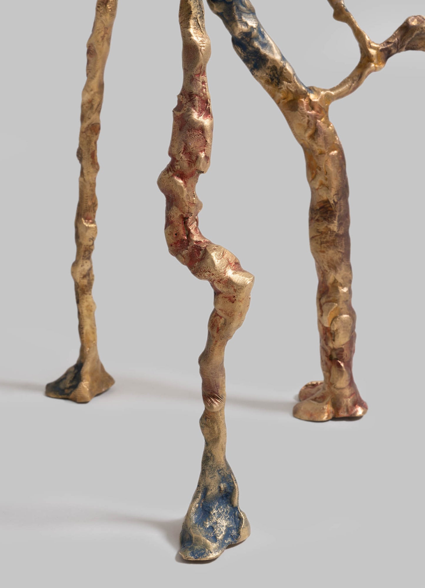 Abstract sculptural art piece made of irregularly shaped metal with a textured, rough surface, finished in a mix of gold, bronze, and blue patina tones. The artwork features organic, twisting forms with a contemporary, handcrafted style.