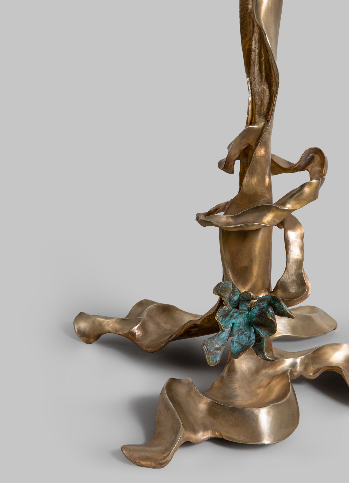 Sculptural art piece made of metal with a polished, reflective finish in a bronze tone, featuring twisting abstract shapes and a textured patina with hints of greenish-blue.