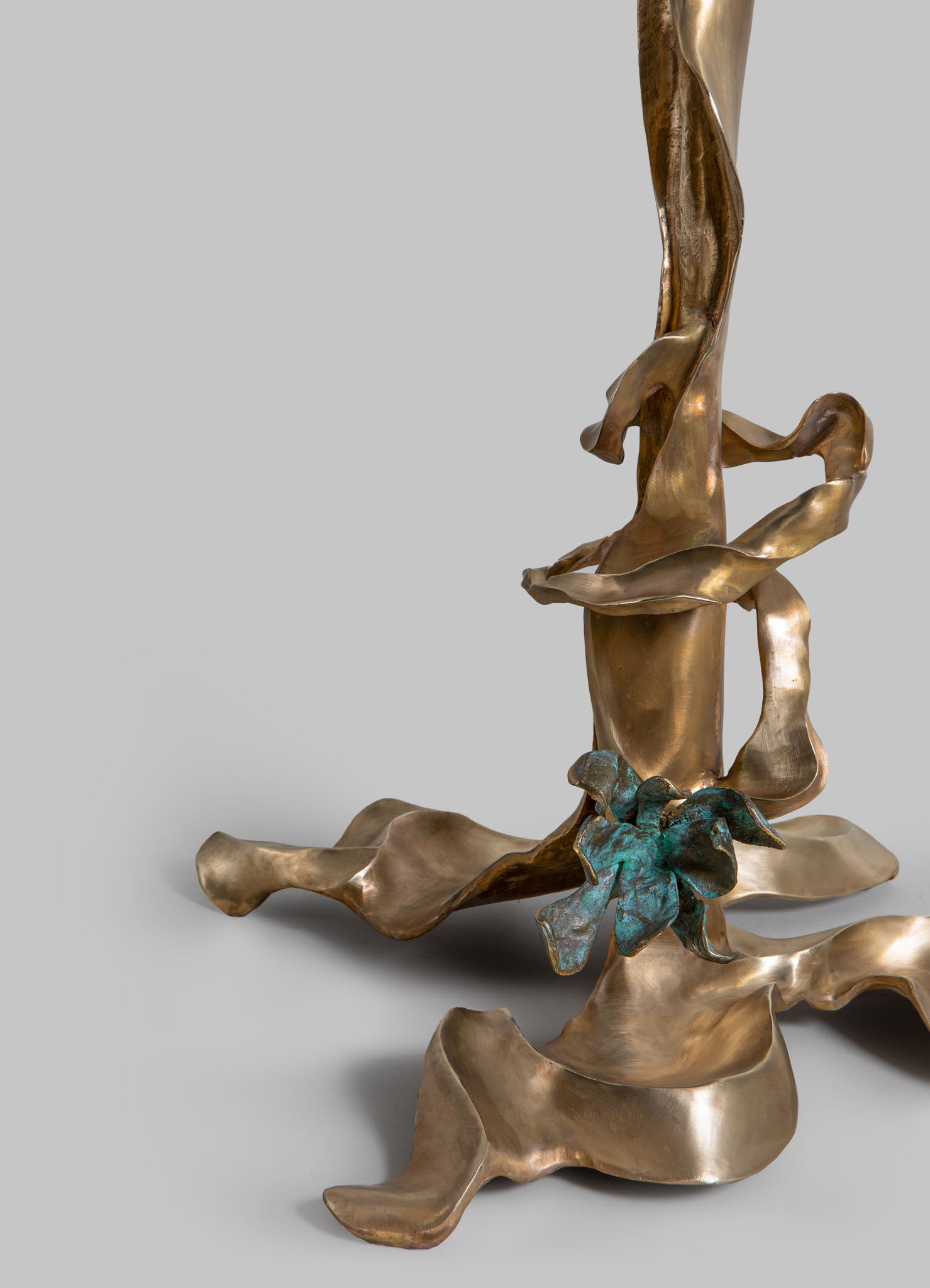Sculptural art piece made of metal with a polished, reflective finish in a bronze tone, featuring twisting abstract shapes and a textured patina with hints of greenish-blue.