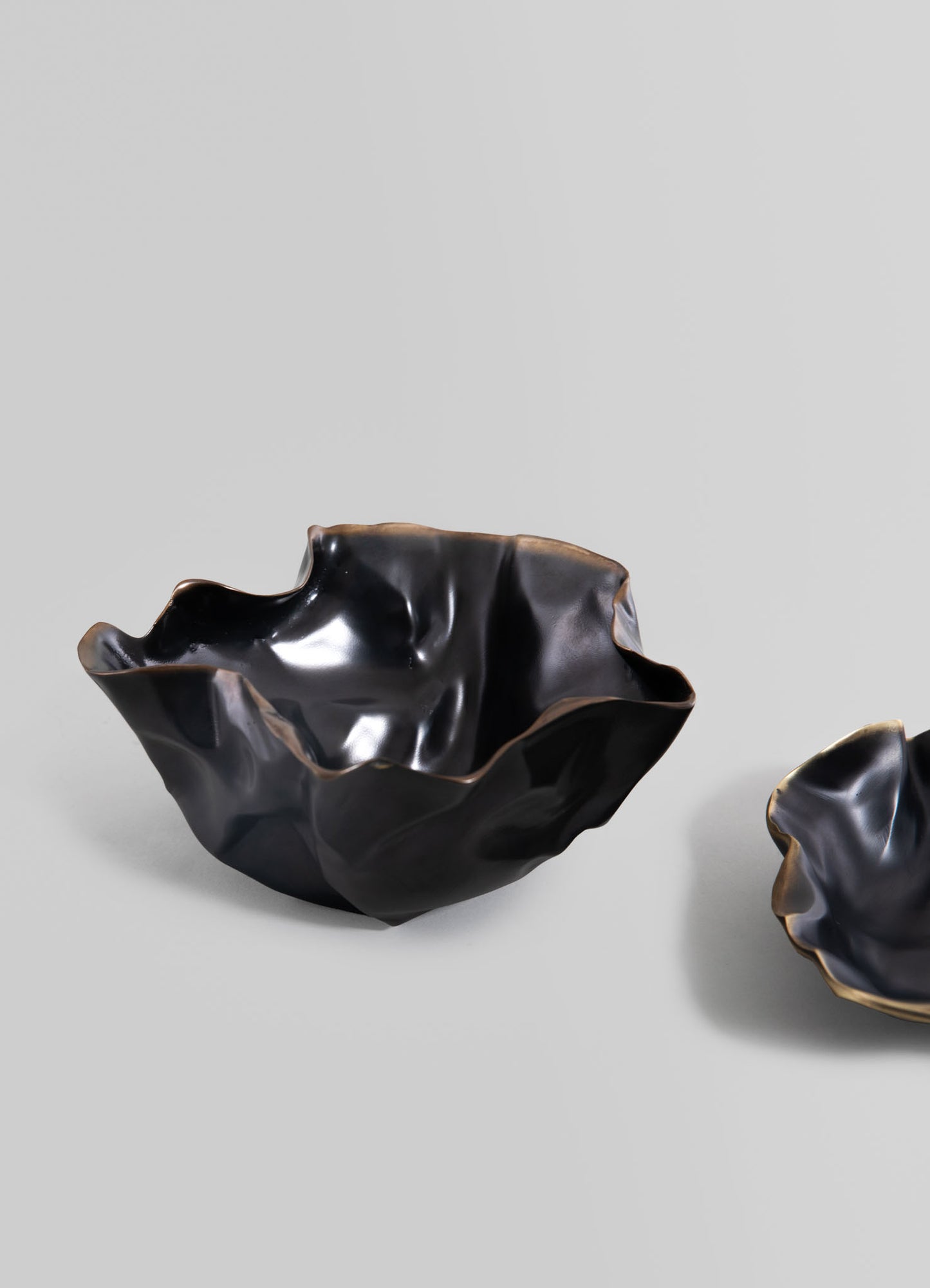 Black ceramic bowls with irregular, organic shapes and a glossy finish, accented with gold trim along the edges. The design evokes a handcrafted, contemporary style.