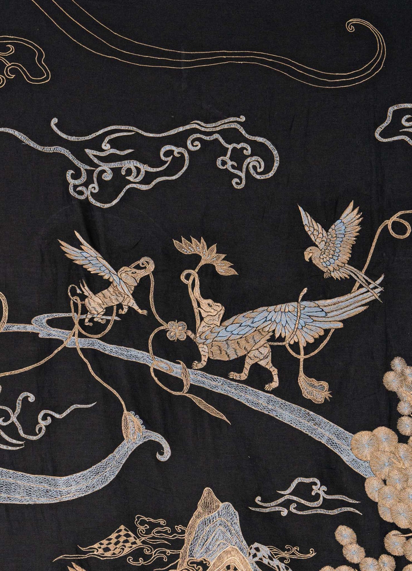 The Dreamscape Black & Gold Embroidered Bedcover by Viya features two mythical birds on floral branches, with swirling clouds and stylized mountains in gold and light blue thread, set against a black background.