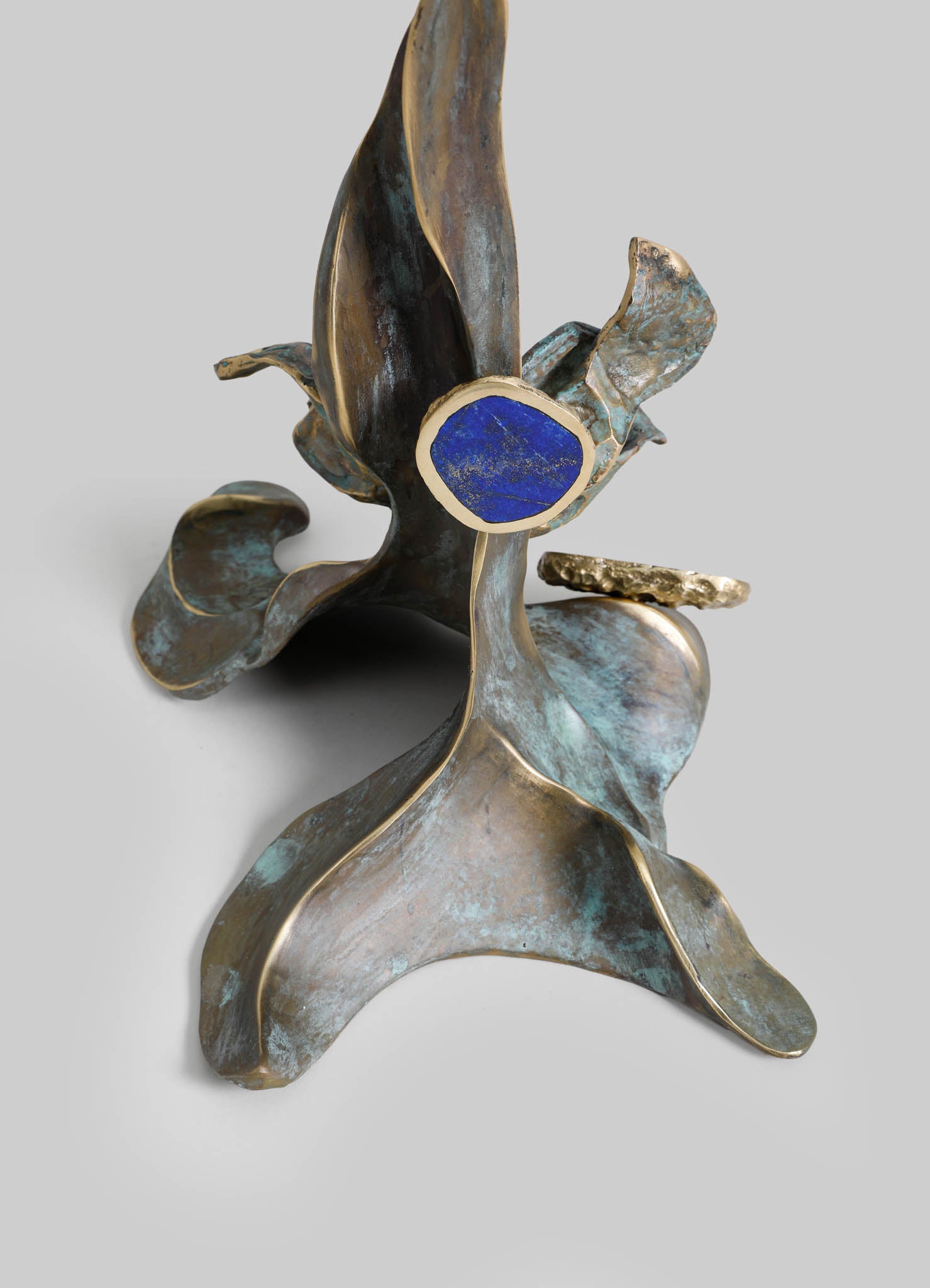 Metal sculpture with abstract, flowing shapes in weathered bronze finish and a blue enamel or stone accent, featuring a contemporary and organic design motif.