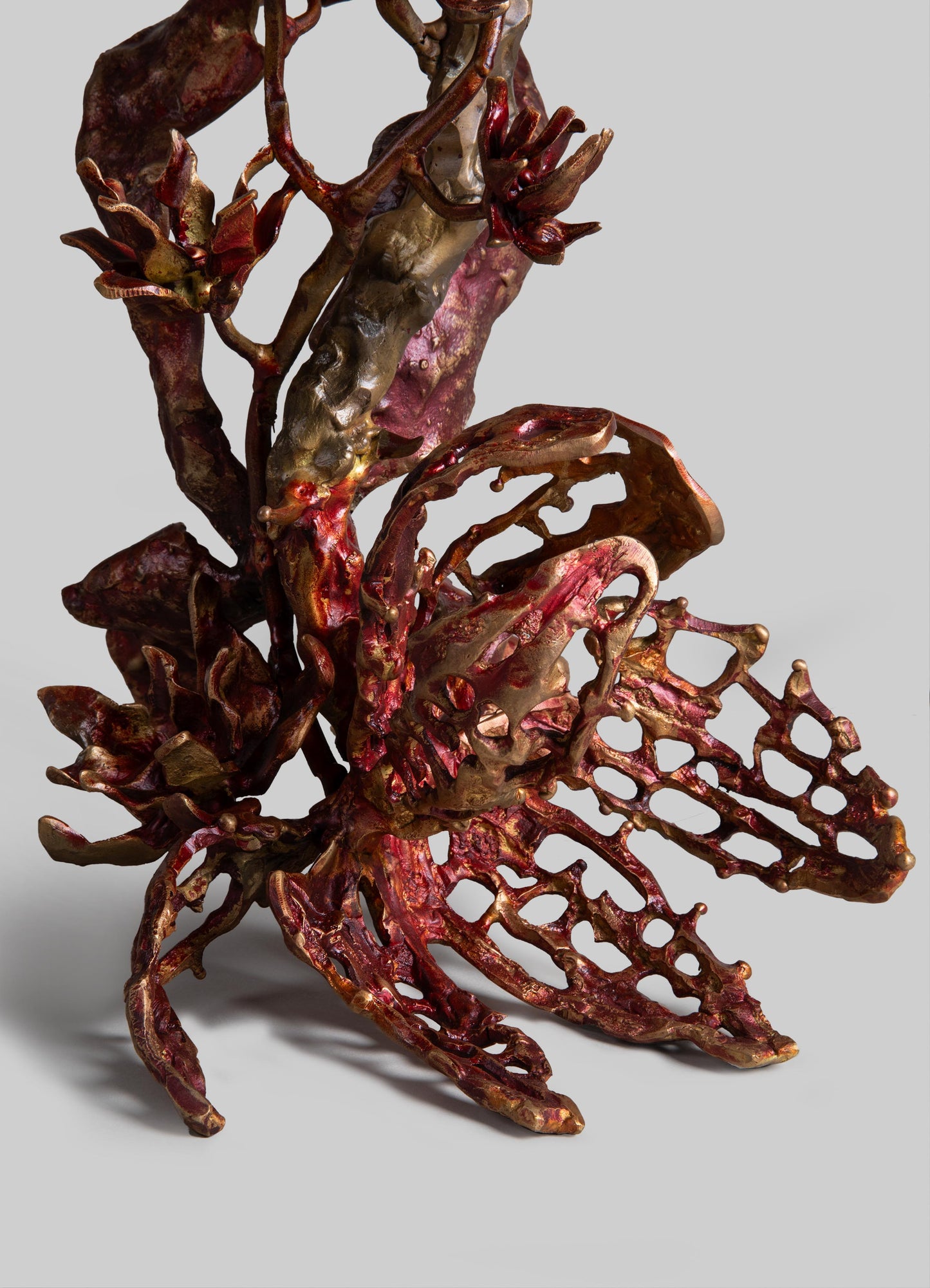 A decorative metal sculpture resembling a butterfly with intricate openwork wings in bronze, red, and gold tones, featuring detailed textured surfaces and a polished finish.