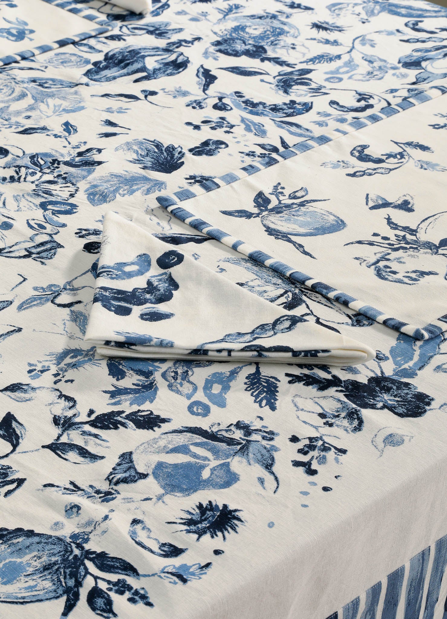 Cotton tablecloth with a blue floral and botanical pattern on a cream background, featuring a striped border for a classic, elegant look.