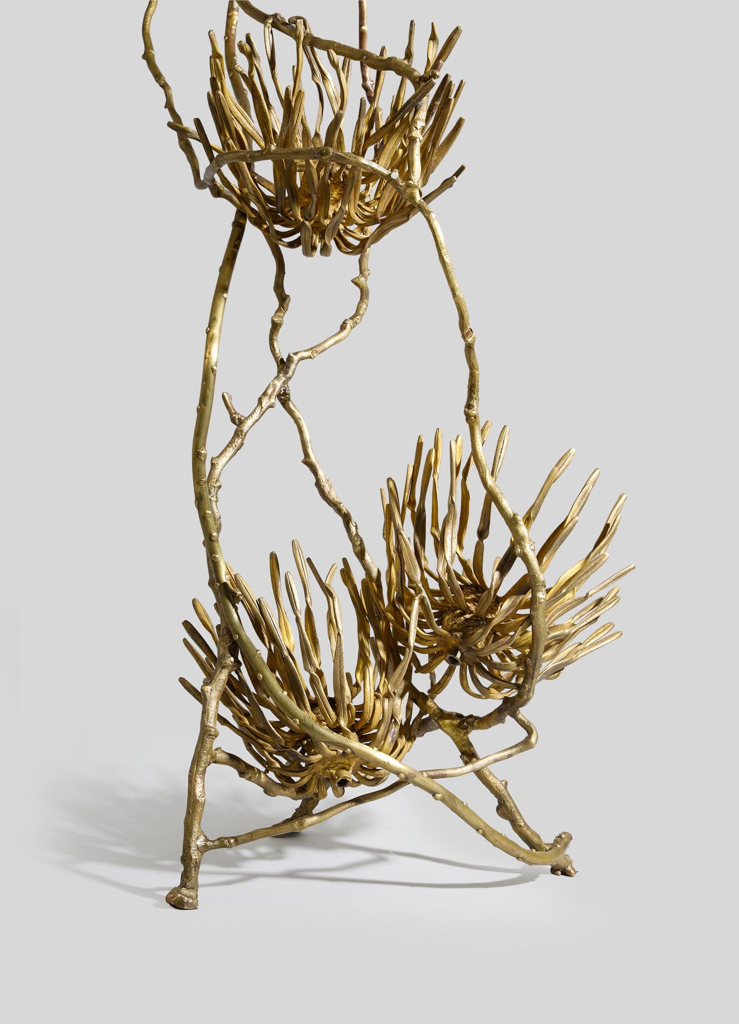 Gold-toned metal sculpture with intertwined, branch-like structures forming two floral motifs, presenting a rustic and contemporary aesthetic. The piece has a textured, handcrafted appearance with an organic, natural-inspired design.