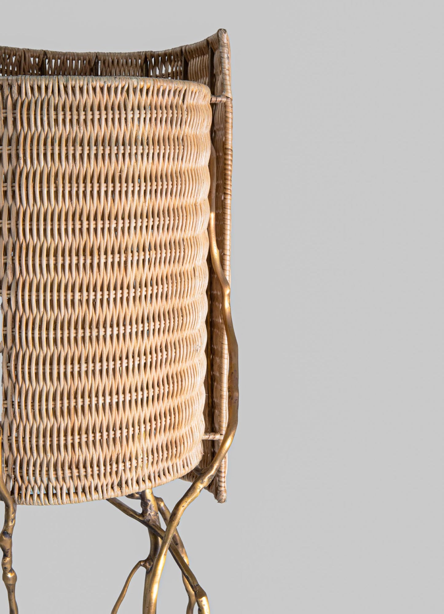 Wicker basket with a rounded, layered weave pattern in natural beige tones, framed by slender metallic gold legs with organic, branch-like shapes. The design combines rustic organic materials with a contemporary gold finish.