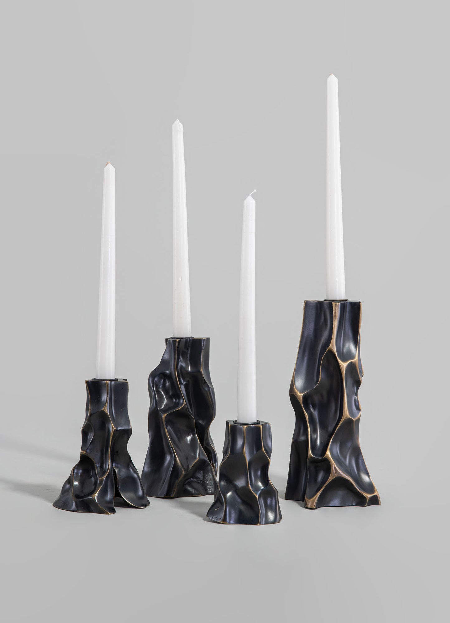 Set of four sculptural candle holders with irregular, organic shapes in black and gold-toned resin, designed to hold taper candles.