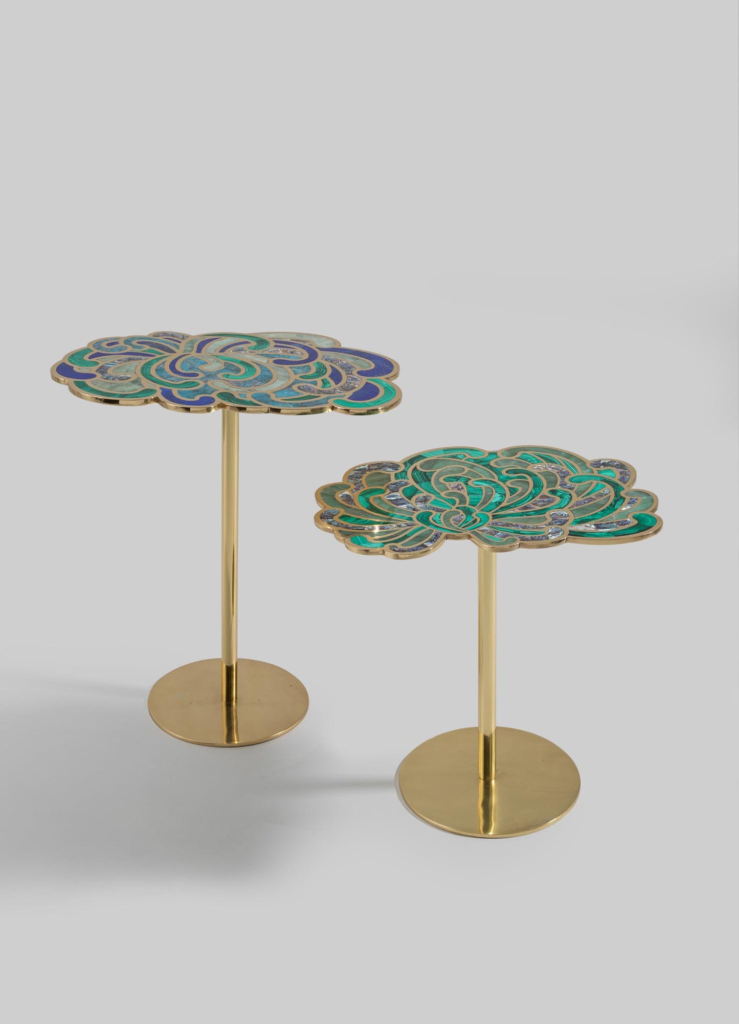 Pair of side tables with mosaic enamel floral motifs in shades of blue, green, and teal, set on cylindrical gold-tone metal bases. The tabletops feature intricate, swirling patterns with a glossy finish, reflecting an artistic, contemporary style.