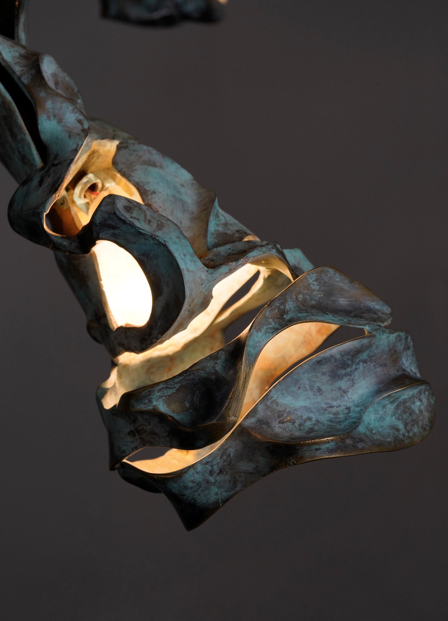 A metal wall sconce with an organic, sculptural design resembling twisted leaves or petals, finished in oxidized brass with a dark patina and warm internal lighting.