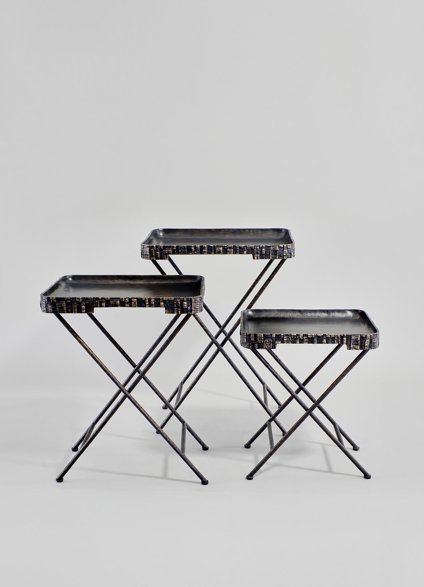 Set of three black metal nesting trays with textured edges and slim, angled legs, arranged on a plain background.