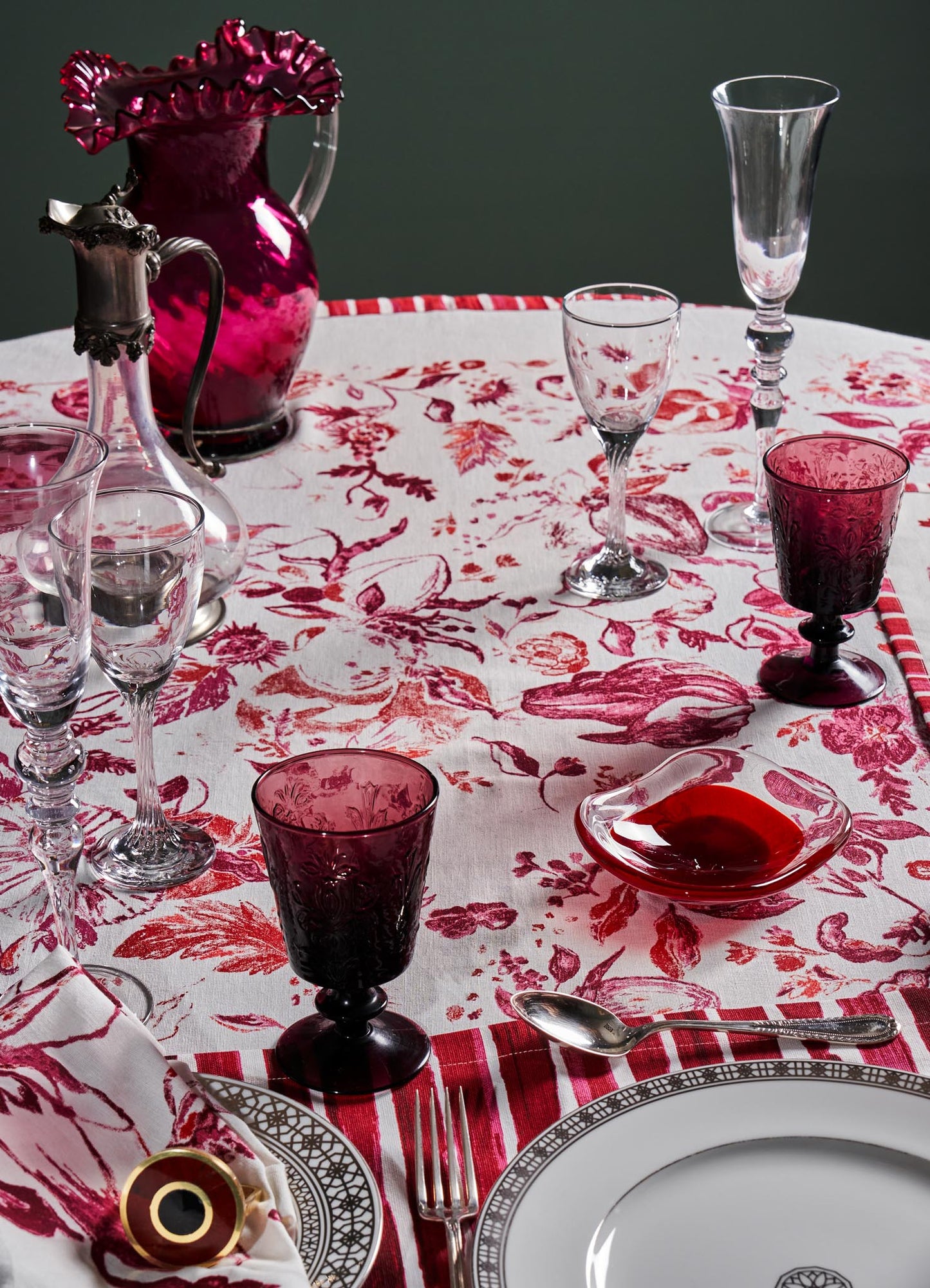 Glassware set including clear and tinted goblets with intricate floral and geometric patterns, arranged on a table with a red and white floral patterned tablecloth.