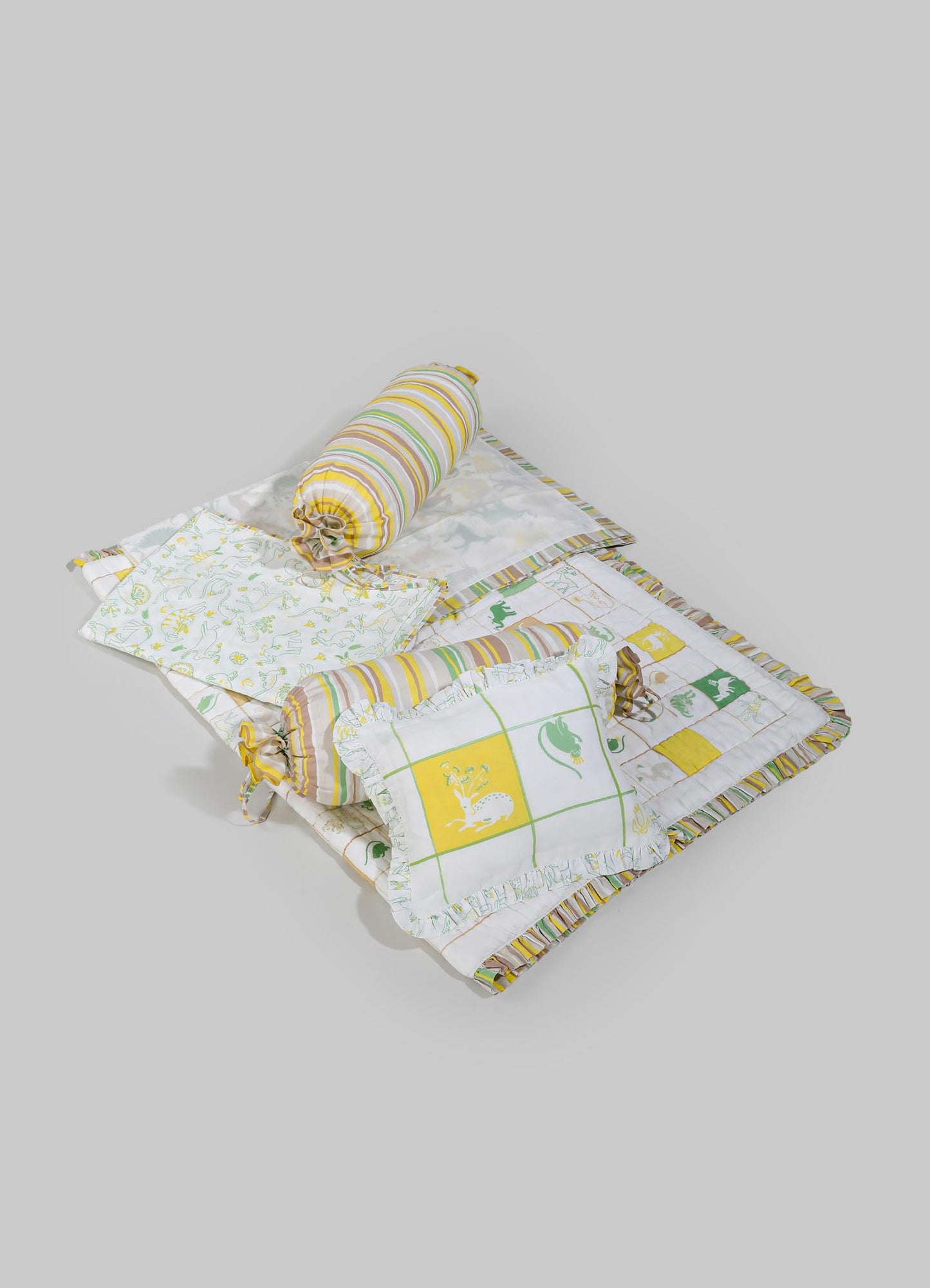 Children's bed set with cotton quilt, pillowcases, and bolster cushions featuring playful dinosaur motifs in green, yellow, and white. The bedding has striped and grid patterns, with ruffled edges and fabric ties, creating a whimsical and cozy look for a child's room.