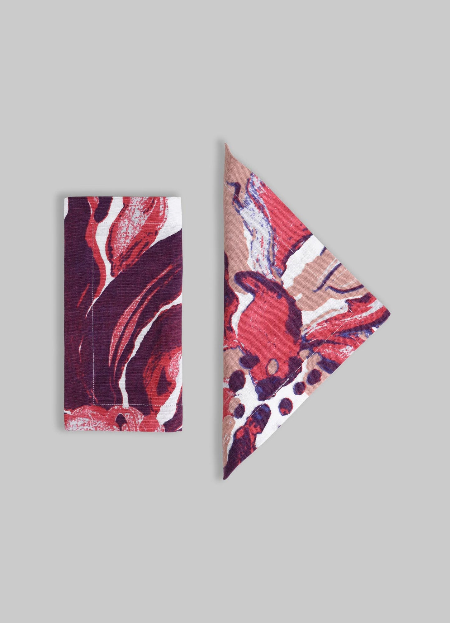 Printed textile accessories featuring abstract floral motifs in shades of red, pink, purple, and white. The set includes a rectangular cloth and a folded napkin or handkerchief with a vibrant, painterly pattern.