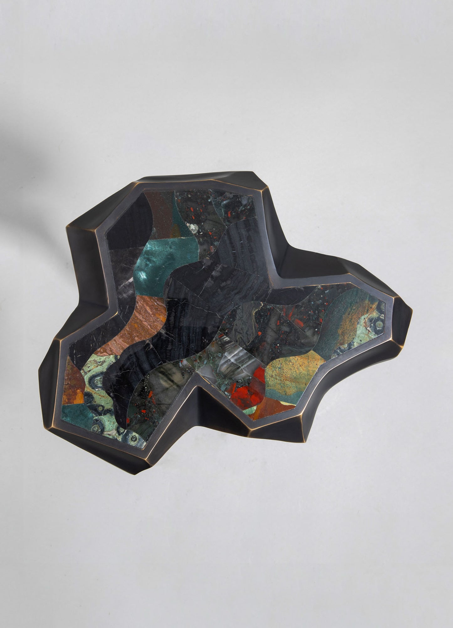 A decorative tray or sculpture with a geometric, irregular shape, featuring a black frame and an inlaid mosaic of colorful stones and marbled patterns in green, orange, red, and dark hues.