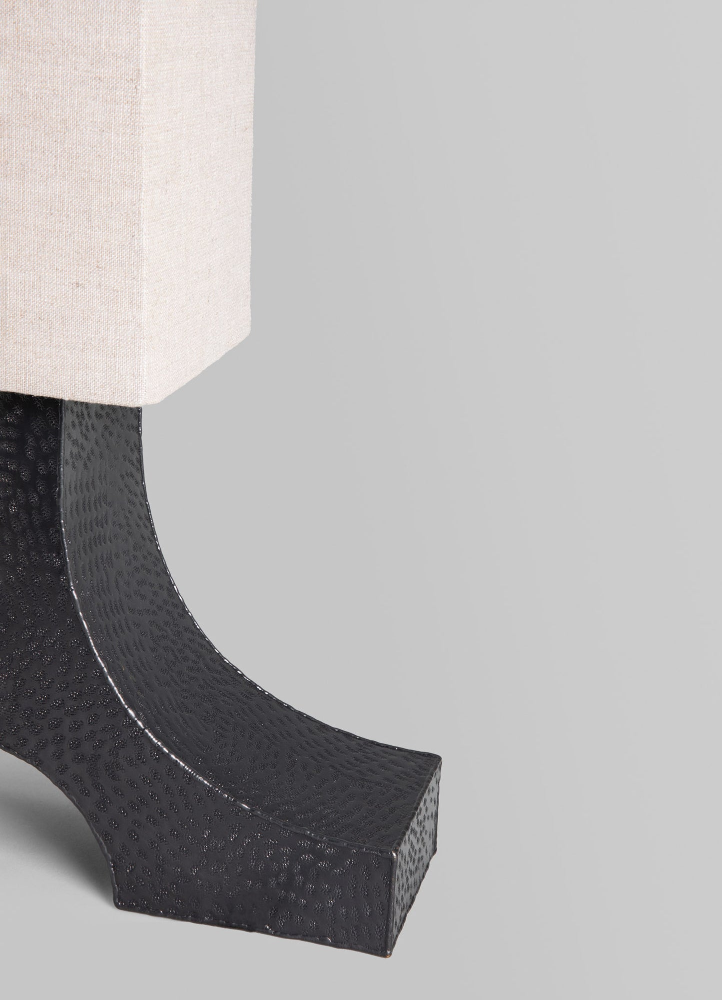 A close-up of a table lamp with a cream fabric lampshade and a black base featuring a textured, dotted pattern and a curved silhouette.