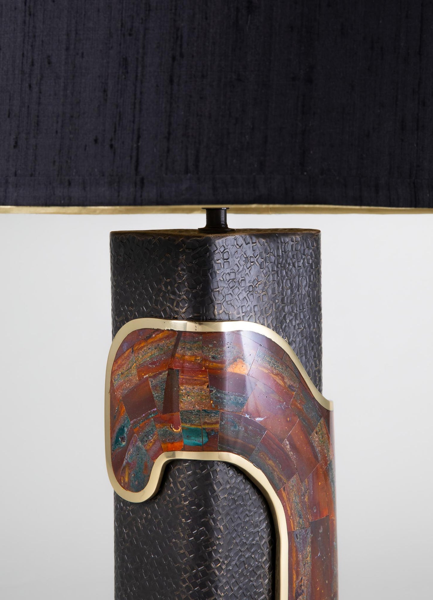 Ceramic table lamp with a textured black body, featuring a multicolored, abstract patterned band with earthy tones and a glossy finish, topped with a black fabric drum shade.
