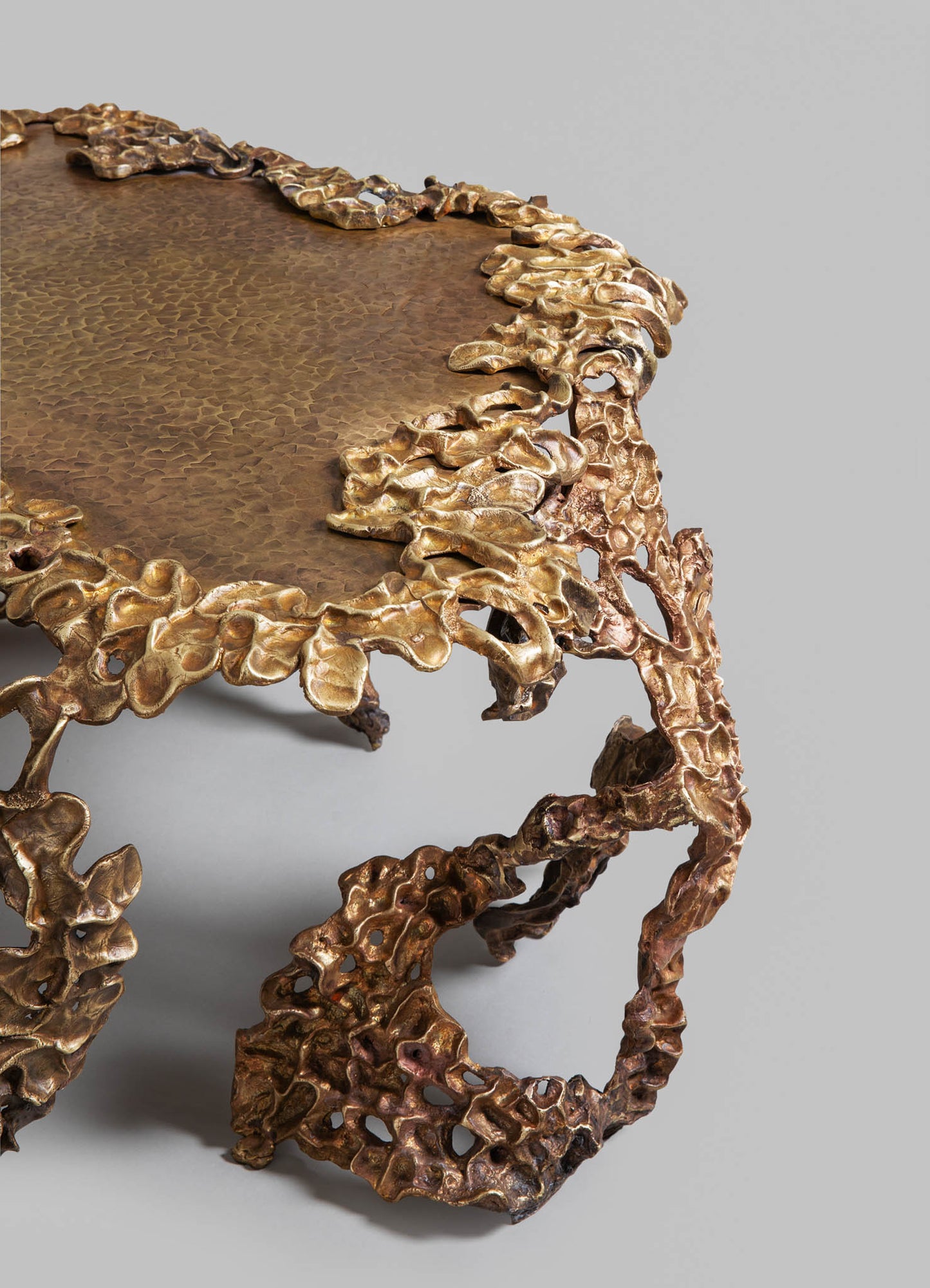 A decorative coffee table with a textured hammered copper surface and an intricate, organic gold-toned metal frame resembling flowing foliage. The design combines rustic craftsmanship with contemporary luxury.