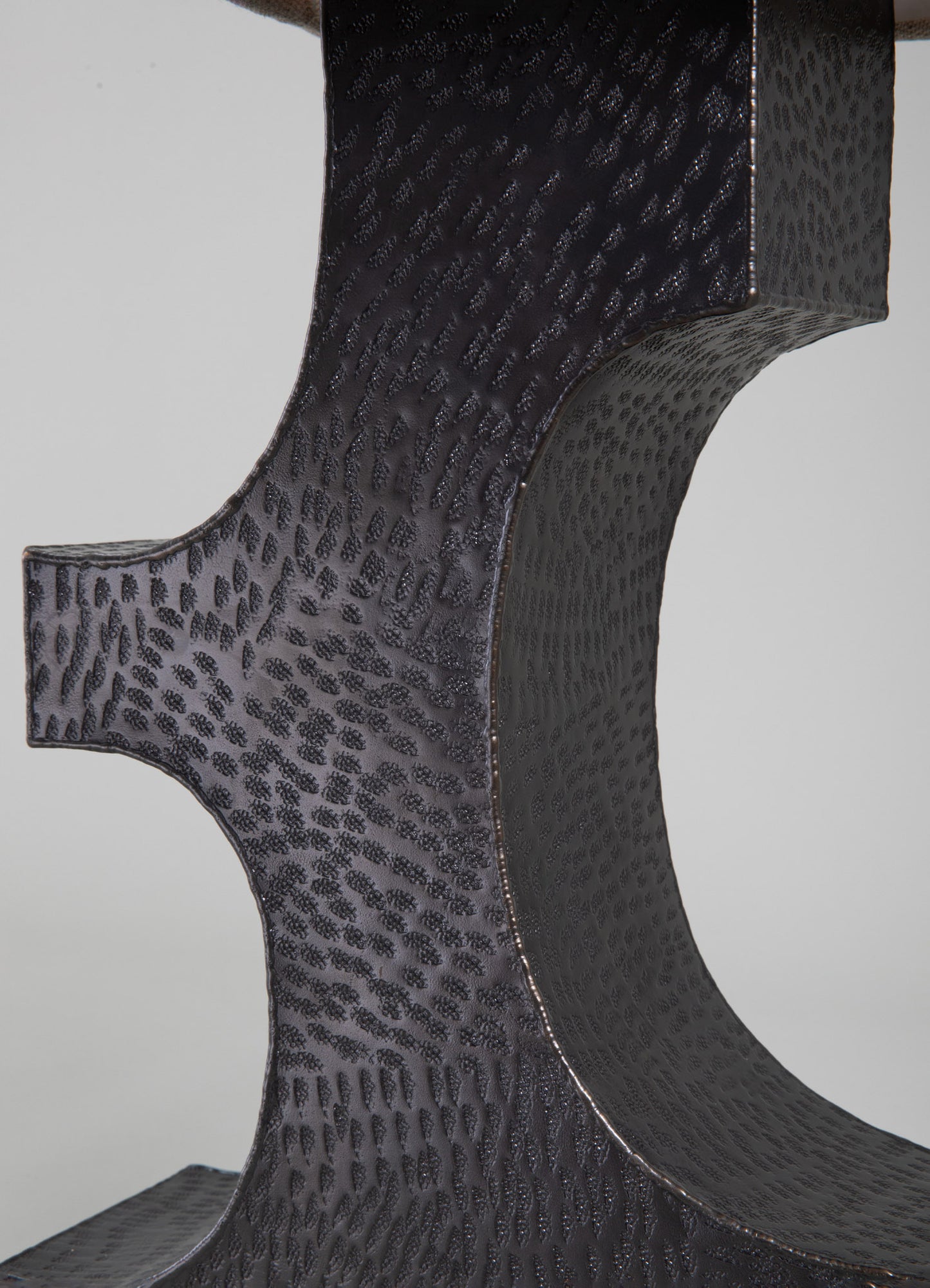 Close-up of a black leather table or furniture piece with a textured, reptile-like pattern and curved edges, featuring a matte finish with subtle sheen and fine stitching along the edges.
