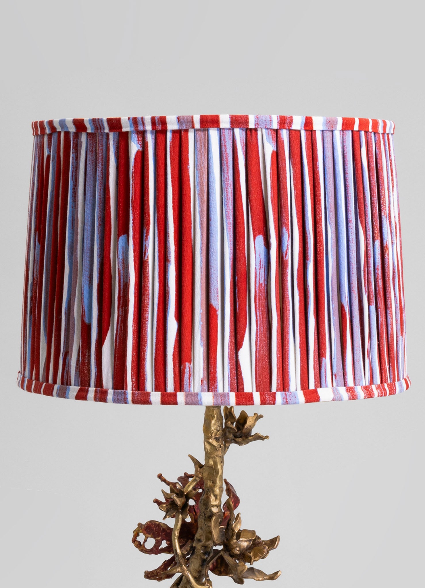 Table lamp with a fabric shade featuring red, white, and blue vertical stripes and pleats, mounted on a base resembling twisted, natural wood or driftwood.