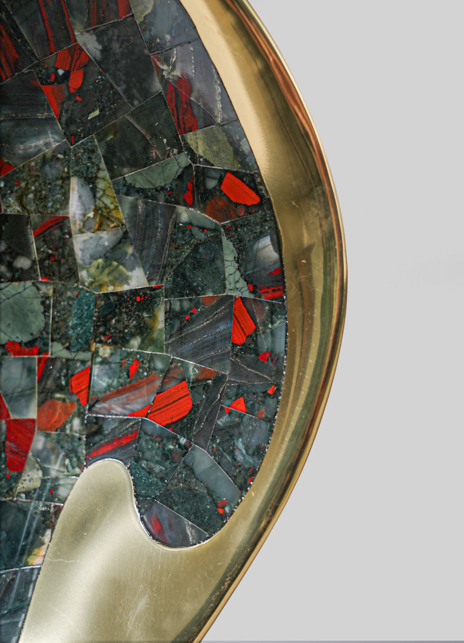 Close-up of a decorative tray with a mosaic surface featuring irregular pieces of black, green, and red stones or glass, set within a metallic gold or brass frame. The tray has an elegant, contemporary style with a polished finish.