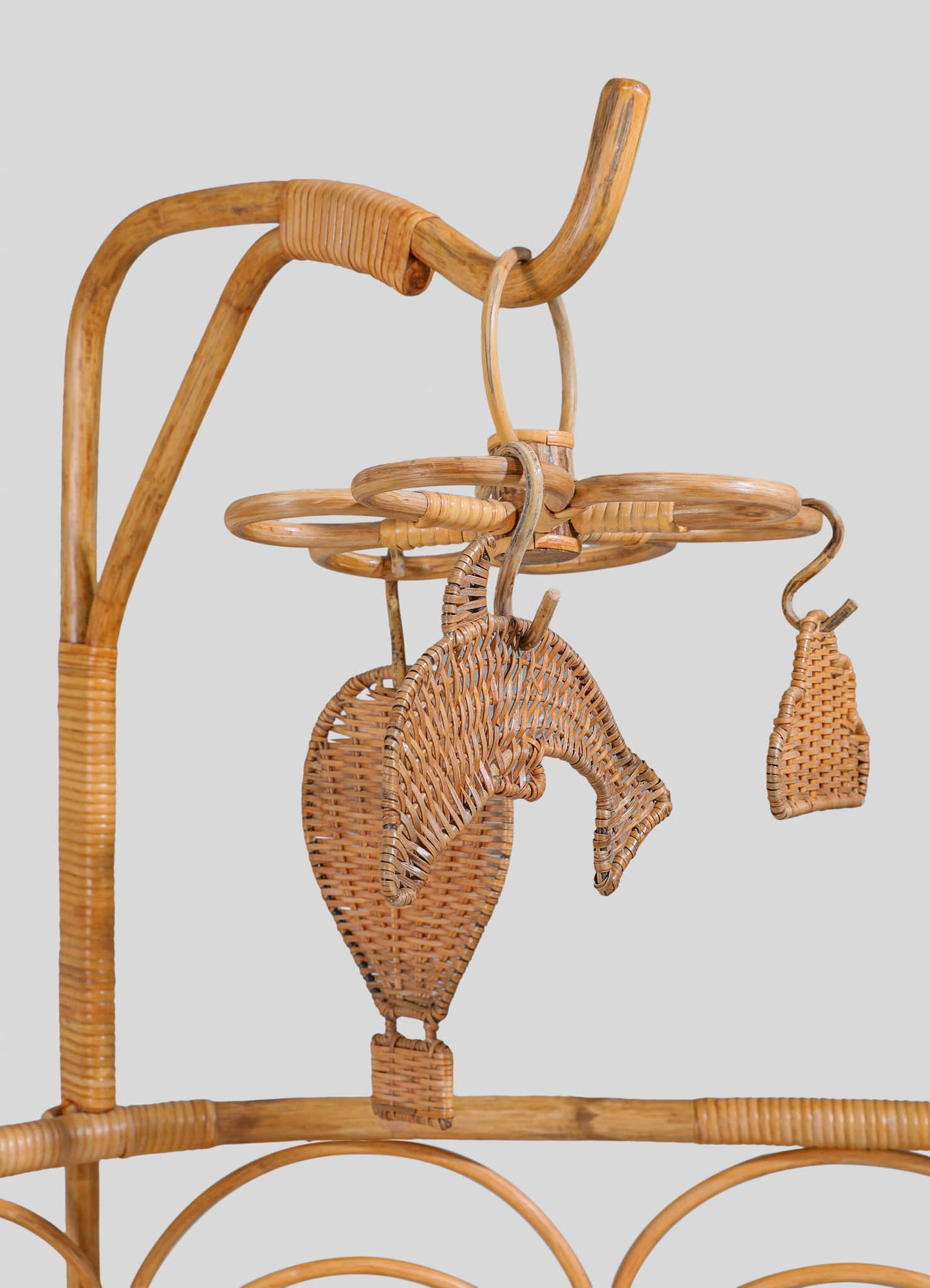 Wicker jewelry stand with a circular top and hanging hooks, crafted from natural woven rattan in a rustic style. The stand features a dolphin-shaped motif and small woven pouch, emphasizing handcrafted detailing.