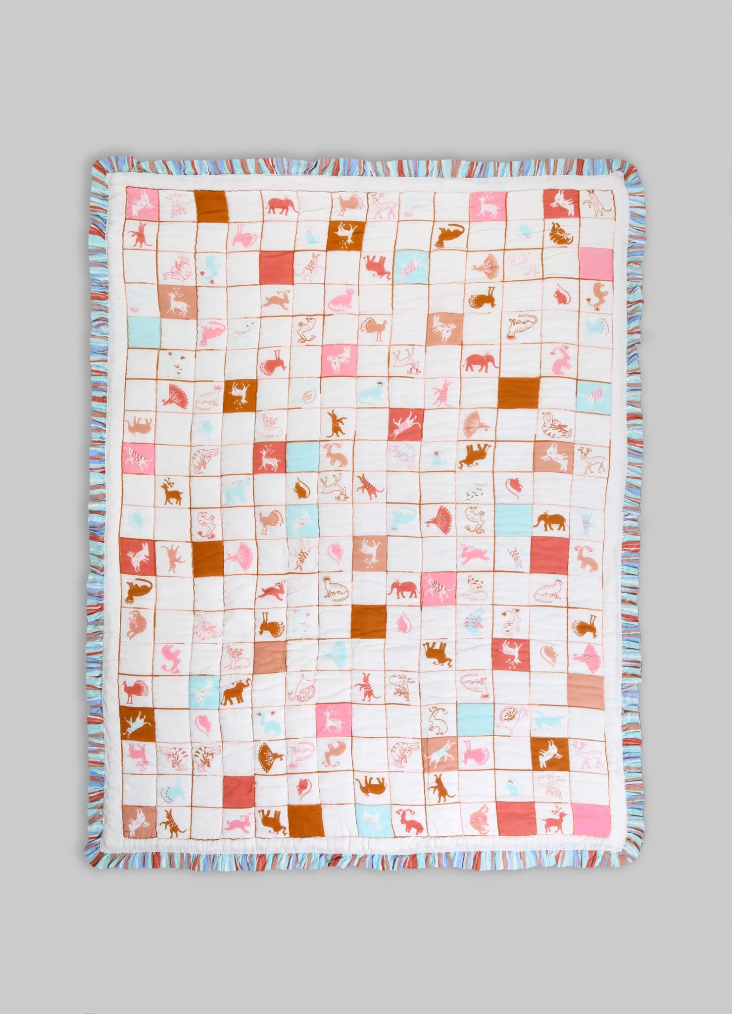 Quilt made of soft cotton fabric featuring a playful animal motif with pink, orange, and light blue colors, bordered with a ruffled striped trim in similar pastel tones.