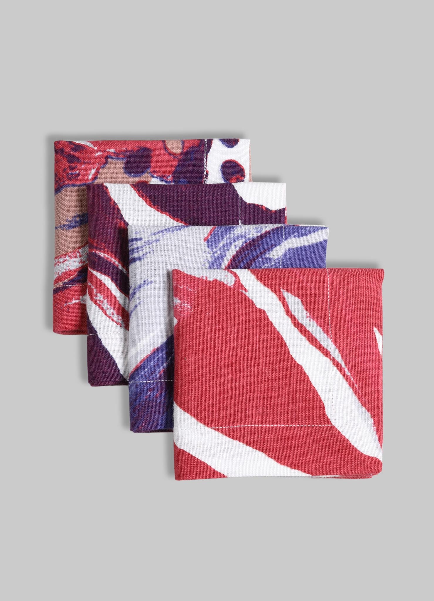 Set of four fabric napkins with abstract floral and brushstroke patterns in bold red, purple, white, and beige tones. Made of cotton or similar material, featuring vibrant colors and large, expressive motifs.