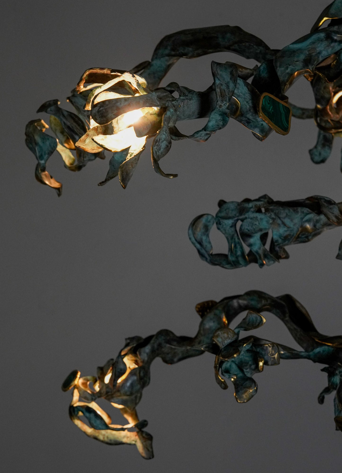 Decorative metal chandelier with an organic, twisted form and a dark patina finish, featuring integrated light sources that emit warm illumination.