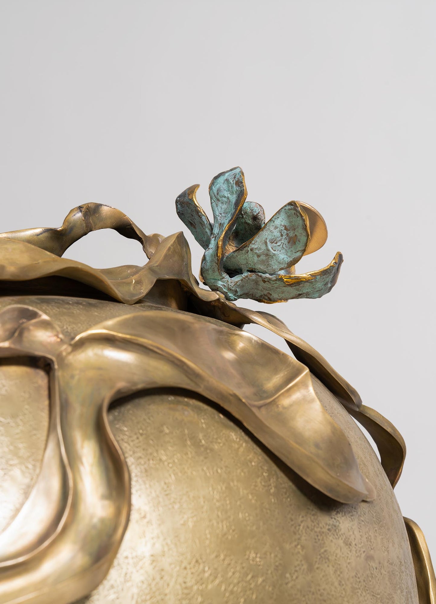 Decorative sculpture featuring a floral motif with a textured, oxidized greenish-blue finish and gold accents on metal petals and leaves. The piece combines organic shapes with a rustic, handcrafted style, suitable for interior decor.